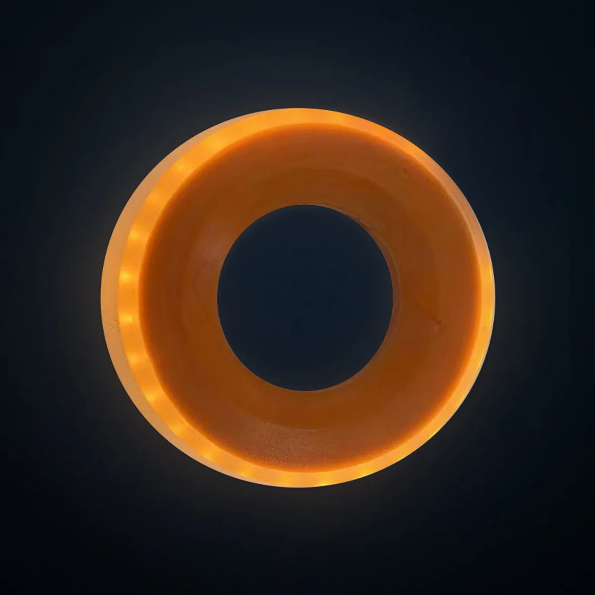 GLACILIT LED ringette ring: orange shell with its amber LEDs lit, on a dark studio backdrop